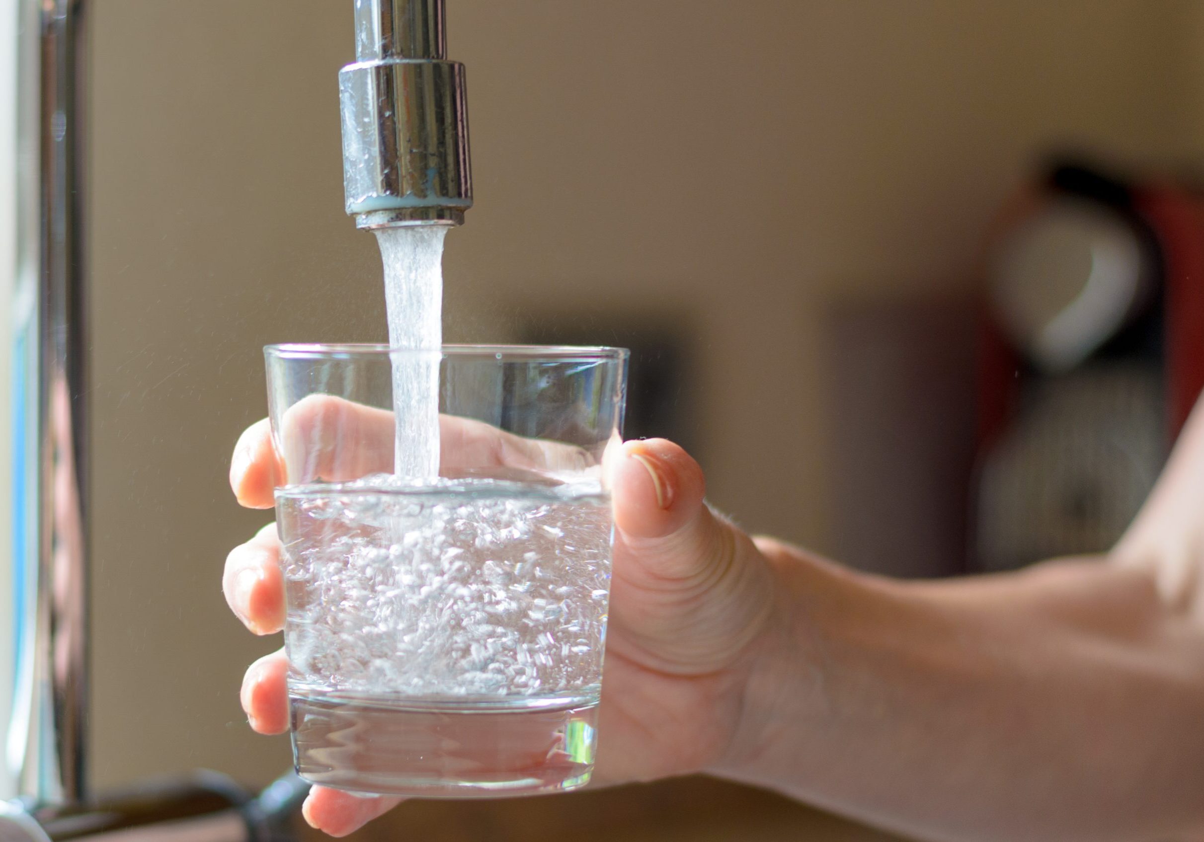 Woman filling a glass of water from a stainless steel or chrome tap or faucet, close up on her hand and the glass, half full