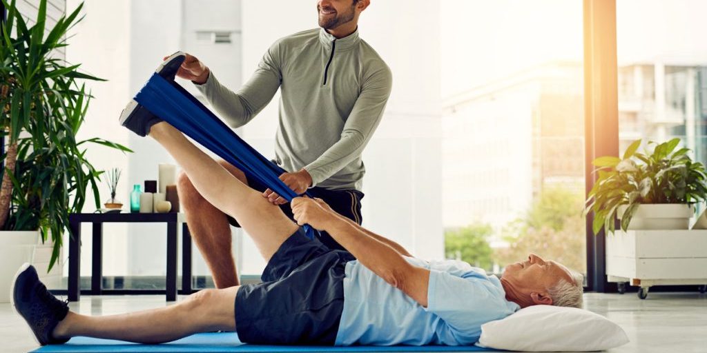 Shot of a physiotherapist helping a senior patient stretch his legs with a stretch band in his office